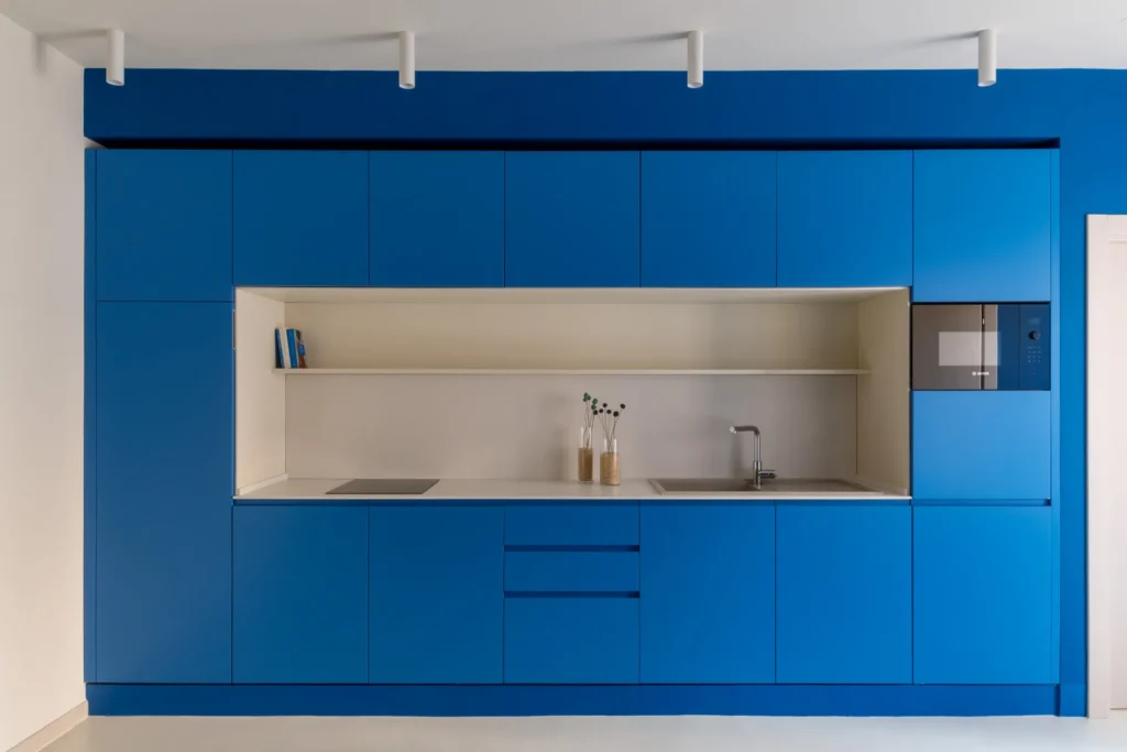 Cucina moderna incassata monoblocco blu con nicchia bianca, faretti a soffitto e design minimalista per casa vacanze.