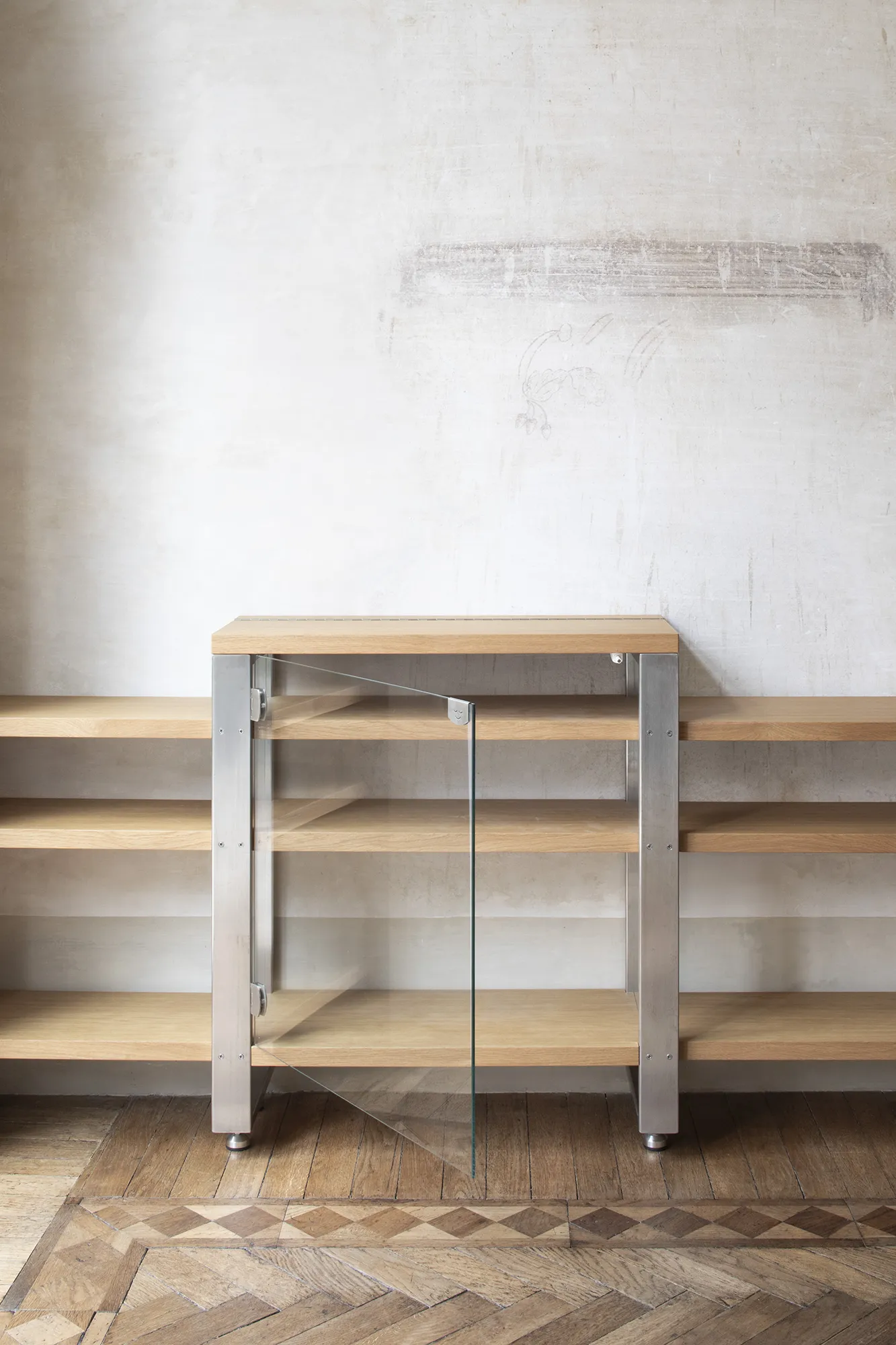 Dettaglio di una credenza moderna su misura con anta in vetro temperato, ripiani in rovere e struttura in acciaio inox satinato.