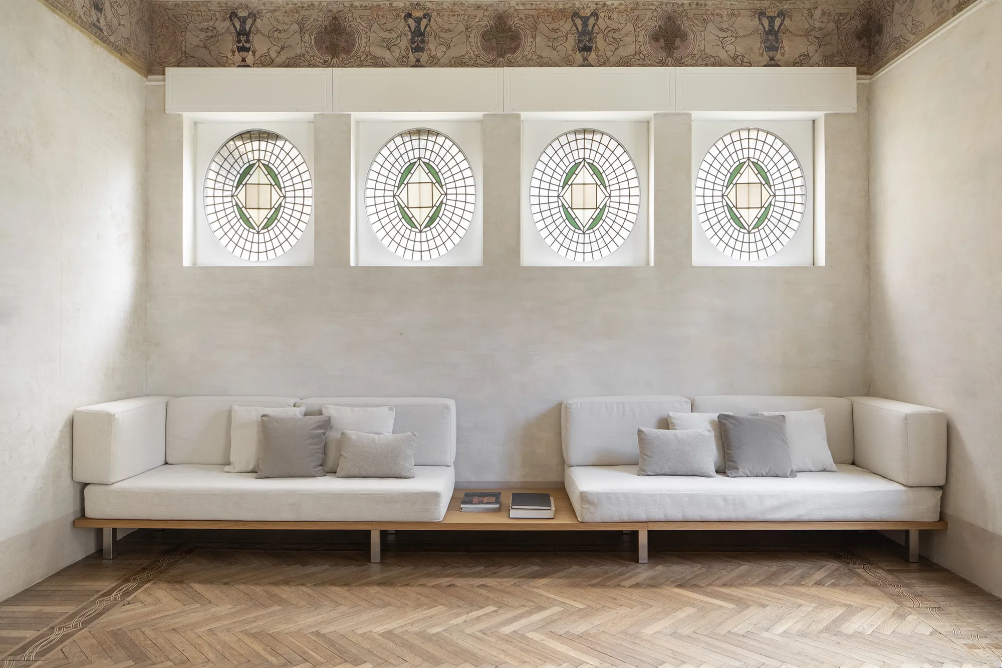 Salone moderno in palazzo storico con quattro finestre a oblò decorate di epoca liberty , fregio affrescato e divani minimalisti su misura su pedana in legno.