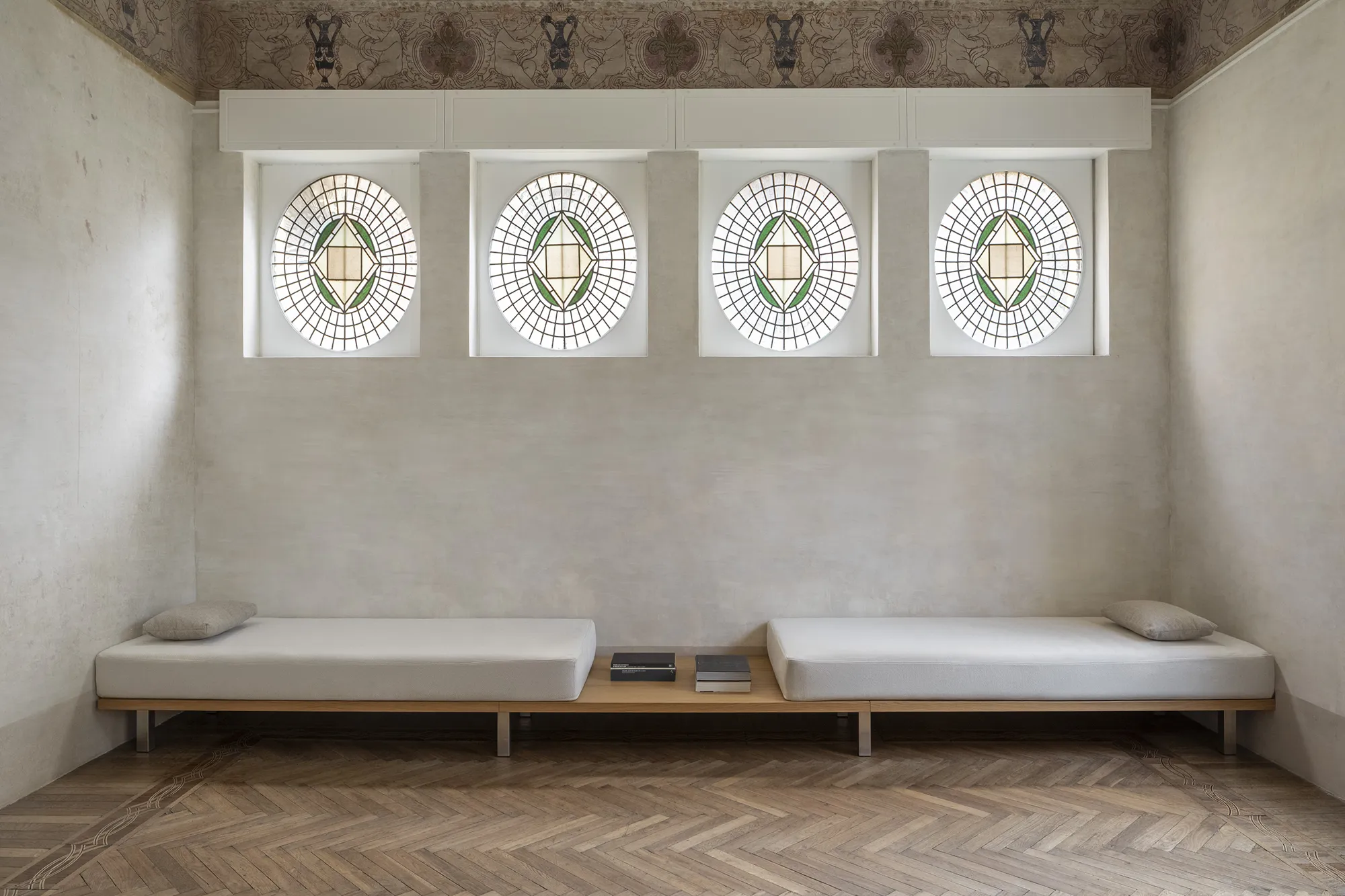 Salone moderno in palazzo storico con quattro finestre a oblò decorate di epoca liberty , fregio affrescato e divani minimalisti su misura su pedana in legno.