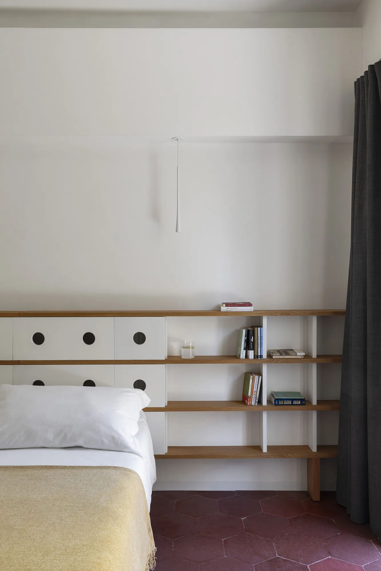 Testiera del letto moderna integrata in una scaffalatura in legno con moduli bianchi a oblò e lampade a sospensione minimali.